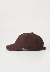 Casquette de baseball rouge foncé avec un motif géométrique noir, visière incurvée et sangle ajustable à l'arrière, présentée de côté sur un fond uni.