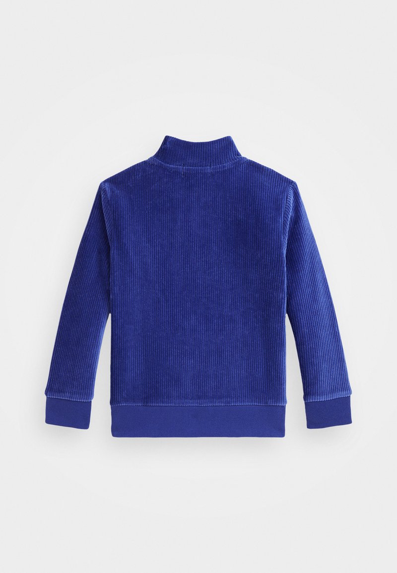 Sudadera de pana azul con un alto cuello, textura acanalada y mangas largas. Presenta un color sólido en todo el diseño y puños elásticos.