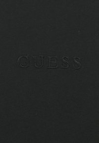 Černé bavlněné tričko s vyraženým logem "GUESS". Hladká textura, přiléhavý střih a žádné další viditelné vzory nebo akcenty.