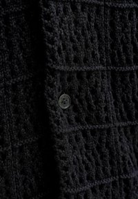 Μαύρο πλεκτό ύφασμα με ραμμένο κουμπί σε υφασμάτινο ένδυμα με υφή βάφλας, κοντινή λήψη.