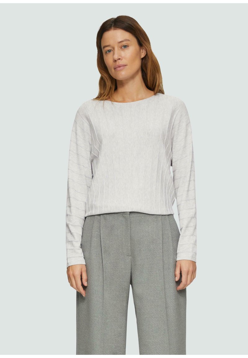 Hellgrau langärmliges Top mit strukturiertem, geripptem Design. Kombiniert mit hoch taillierten, weit geschnittenen grauen Hosen. Minimalistischer, moderner Stil.