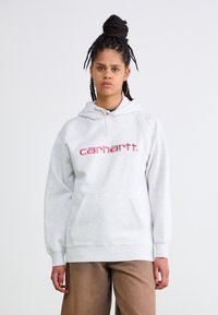 Felpa grigia realizzata in tessuto morbido, con tasca frontale e cappuccio con coulisse. Logo "carhartt." rosso stampato in modo prominente sul petto.