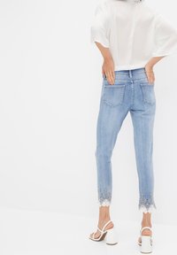 Světlé modré džíny z denimu s krátkým střihem a krajkovým lemem. Obsahují dvě zadní kapsy a středně vysoký pas.