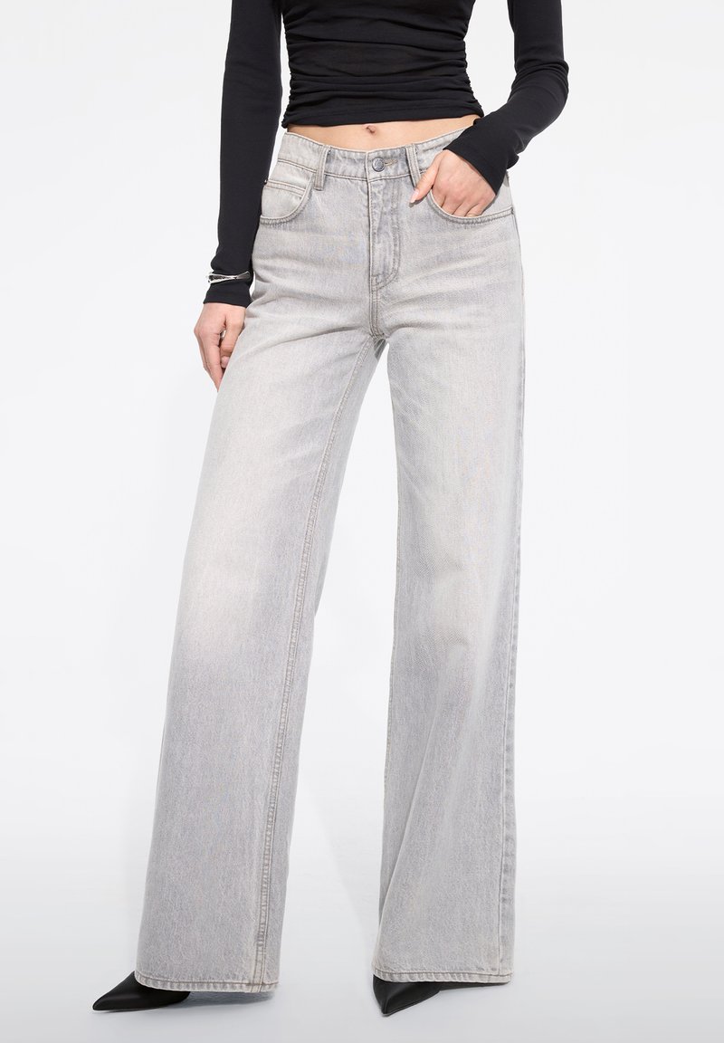 Jeans de pierna ancha gris claro con cintura alta, diseño de cinco bolsillos y dobladillo deshilachado. Combinados con una camiseta ajustada de manga larga negra.