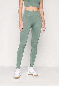 Leggings verdes acanalados con una cintura alta, combinados con zapatillas deportivas blancas. Textura suave, diseño ajustado para ropa deportiva.