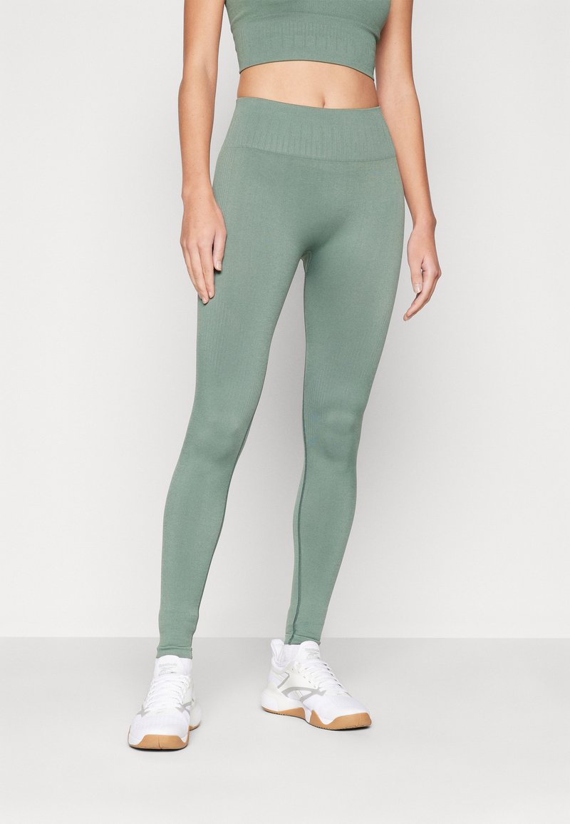 Leggings verdes acanalados con una cintura alta, combinados con zapatillas deportivas blancas. Textura suave, diseño ajustado para ropa deportiva.