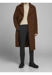 Brauner Wollmantel mit doppelter Knopfleiste, beigem Rollkragenpullover, grauen karierten Hose und schwarzen Schnürstiefeln. Glatte Textur.