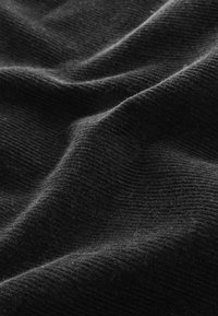 Gros plan d’un tissu côtelé noir doux avec une texture visible et des plis doux créant des variations de lumière et d’ombre.