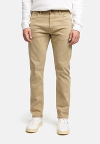 Pantalones de algodón chambray beige con un corte recto, que cuentan con bolsillos estándar, cierre de botón y cremallera. Combinados con zapatillas blancas.