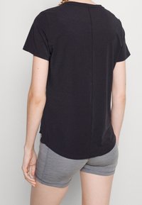 Svart t-shirt med kort ärm och rund hals, mjukt material och en något rundad nederkant bak, i kombination med grå shorts.