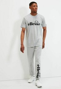 Camiseta de manga corta gris y pantalones de chándal a juego, con un gran logo negro de "ellesse". Tejido suave, corte relajado y escote redondo básico.