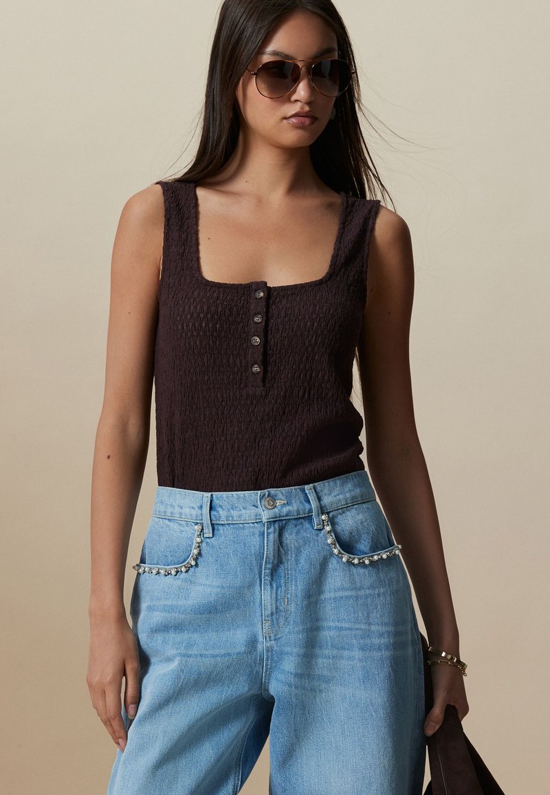 Maiou maro închis, texturat, cu decolteu pătrat și cinci nasturi în față, asortat cu blugi din denim albastru deschis cu buzunare împodobite.