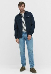 Mörk marinblå jacka med två bröstfickor, bärs över en vit och marinblårandig skjorta. Ljusblå jeans och mörkbruna skor fulländar stilen.