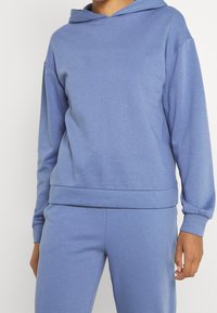 Ljusblå huvtröja i mjukt material; avslappnad passform med ribbad mudd vid ärmar och nederkant; har en känguruficka framtill.