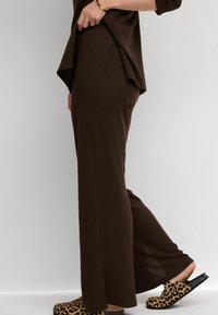 Top marrón de punto acanalado con una abertura lateral, combinado con zuecos de estampado de leopardo con suela negra. Enfocado en un diseño cómodo y de corte holgado.