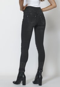 Höga svarta denimjeans med slim fit, med strassdetaljer längs fåll och bakfickor. Texturerad tygdetalj synlig.