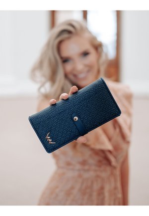 Navy blue wallet with a textured exterior, gold hardware accent, and a button closure. Features a logo in the lower corner.