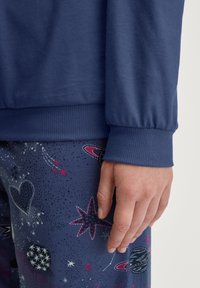 Marineblauwe sweatshirt met geribbelde manchetten, gecombineerd met gestreepte pyjamabroek met sterren en planeten in tinten roze en wit.