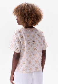 Witte geborduurde blouse met bloemmotieven en een scalloped zoom. Korte mouwen en een textuur, lichte stof. Achteraanzicht weergegeven.