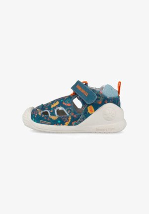 Sandalia para niño pequeño en azul y naranja con patrones de flores y dinosaurios, suela blanca flexible y tira de velcro con la etiqueta "biomecanics".