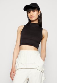 Top cropped preto sem mangas com gola alta, feito de um tecido canelado. Combinado com calças brancas de cintura alta com hardware visível.