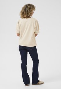 Top beige a maniche a sbuffo con una vestibilità comoda, abbinato a jeans svasati di colore blu scuro e sneakers di colore chiaro. Materiale in cotone morbido, design casual.