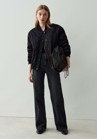 Veste bomber matelassée noire avec boutons-pression, jean noir taille haute, et petit sac à dos noir. Texture lisse, coupe décontractée et design minimal.