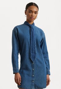 Abito camicia in denim blu scuro, con maniche lunghe, colletto annodato, chiusura frontale con bottoni e una linea dritta con orlo leggermente curvo.