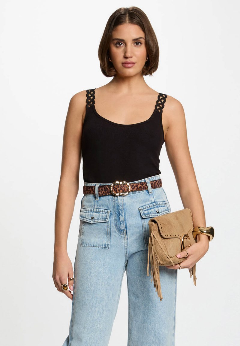 Black tank top with decorative straps, high-waisted light blue denim jeans with pockets, leopard print belt, and a tan fringe handbag.