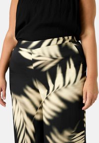 Pantaloni neri e crema con un motivo a foglie di palma, realizzati in tessuto morbido, con una vestibilità sartoriale e una cintura ampia.