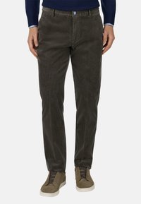 Donkerbruine corduroy broek met subtiele ribbelstructuur, voorzien van een blauwe knop en zijzakken, gecombineerd met olijfgroen sneakers.