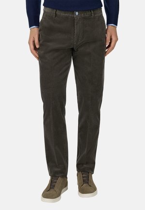 Donkerbruine corduroy broek met subtiele ribbelstructuur, voorzien van een blauwe knop en zijzakken, gecombineerd met olijfgroen sneakers.