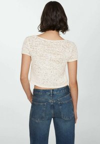 Haut en crochet crème à manches courtes, présentant un design à mailles ouvertes. Assorti à un jean bleu taille haute, mettant en valeur des poches avant et arrière.