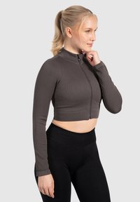 Grijze geribbelde zip-up cropped jas met lange mouwen en hoge kraag, gecombineerd met zwarte high-waisted leggings. Soepele, strakke textuur.