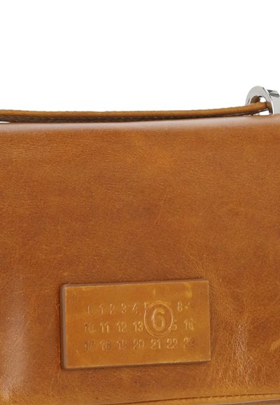 Borsa a tracolla in pelle marrone con una texture liscia, forma rettangolare e un'applicazione in metallo argentato. Presenta un'etichetta identificativa stampata.