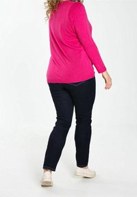 Ihana vaaleanpunainen neule paksuilla hihoilla yhdistettynä tummansinisiin farkkuihin. Neuleessa on sileä pinta, ja asusteena on valkoiset kengät.