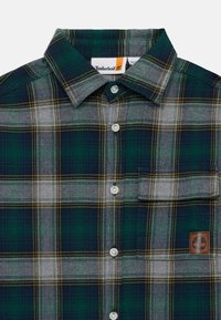 Grønn, grå og marineblå rutete knappskjorte med frontlomme på brystet og Timberland-logo på nedre høyre side.