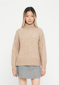 Beige kötött pulóver, magas gallérral, bordás mandzsettával és szegéllyel, puha tapintással. Szürke filcből készült mini szoknyával párosítva.
