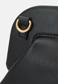 Coin de sac en cuir noir avec une finition texturée, mettant en avant un anneau en métal doré et un détail de couture visible le long de la couture.