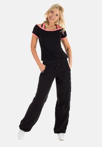 Black athletic top with pink accents, fitted at the waist, paired with loose black pants featuring side pockets and drawstring. White sneakers.
