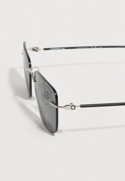 Ορθογώνια γυαλιά ηλίου με μαύρο πλαίσιο, λεπτούς μεταλλικούς βραχίονες και σκουρόχρωμους φακούς, εμφανιζόμενα σε λευκό φόντο.