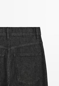 Vista posteriore di jeans in denim nero che mostrano la vita con passanti per la cintura e due tasche posteriori su uno sfondo bianco.