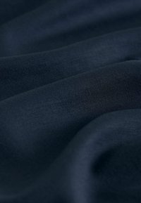 Dunkelblauer Stoff mit sanften Falten und feiner Strickstruktur, die die glatten und flexiblen Eigenschaften des Materials hervorhebt.