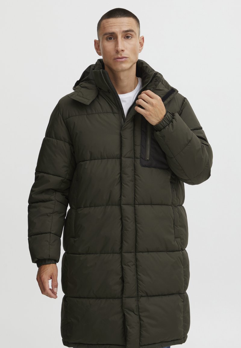 Pūķa mētelis tumši zaļā krāsā, ar quilted tekstūru, regulējamu kapuci un melnu rāvējslēdzēja kabatu uz krūšu. Garas piedurknes un priekšējais rāvējslēdzējs.