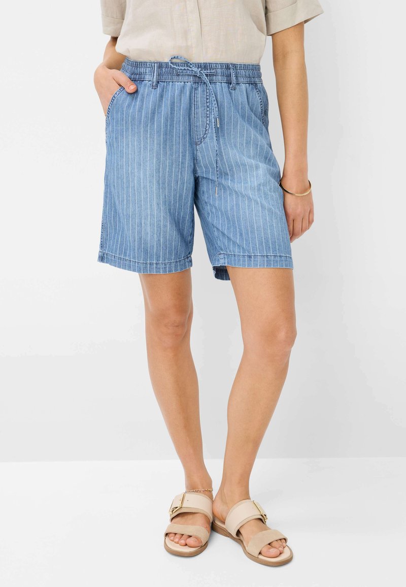 Shorts in denim di un blu chiaro con strisce bianche verticali, vita elastica con cordino e tasche laterali. Indossati con sandali color sabbia.