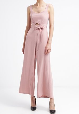 Une combinaison sans manches rose avec un col carré, une ceinture en tissu et un détail de découpe à l'avant. Design à jambes larges et texture lisse. Escarpins noirs.