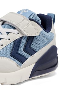 Blå och vita sneakers med en texturerad mesh-ovandel, läderdetaljer, en kardborreband och en tjock marinblå sula med ett mönstrat design.