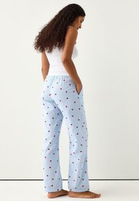 Γαλάζιες ριγέ πιτζάμες με κόκκινα λουλούδια, με ελαστική μέση και πλαϊνές τσέπες. Το ύφασμα φαίνεται μαλακό και ελαφρύ.