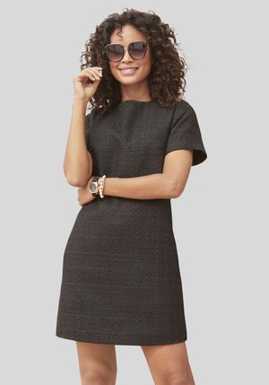 Zwarte textuurovergang met korte mouwen en een ronde halslijn, met een getailleerde silhouet. Model isaccessorized met oversized zonnebrillen en armbanden.