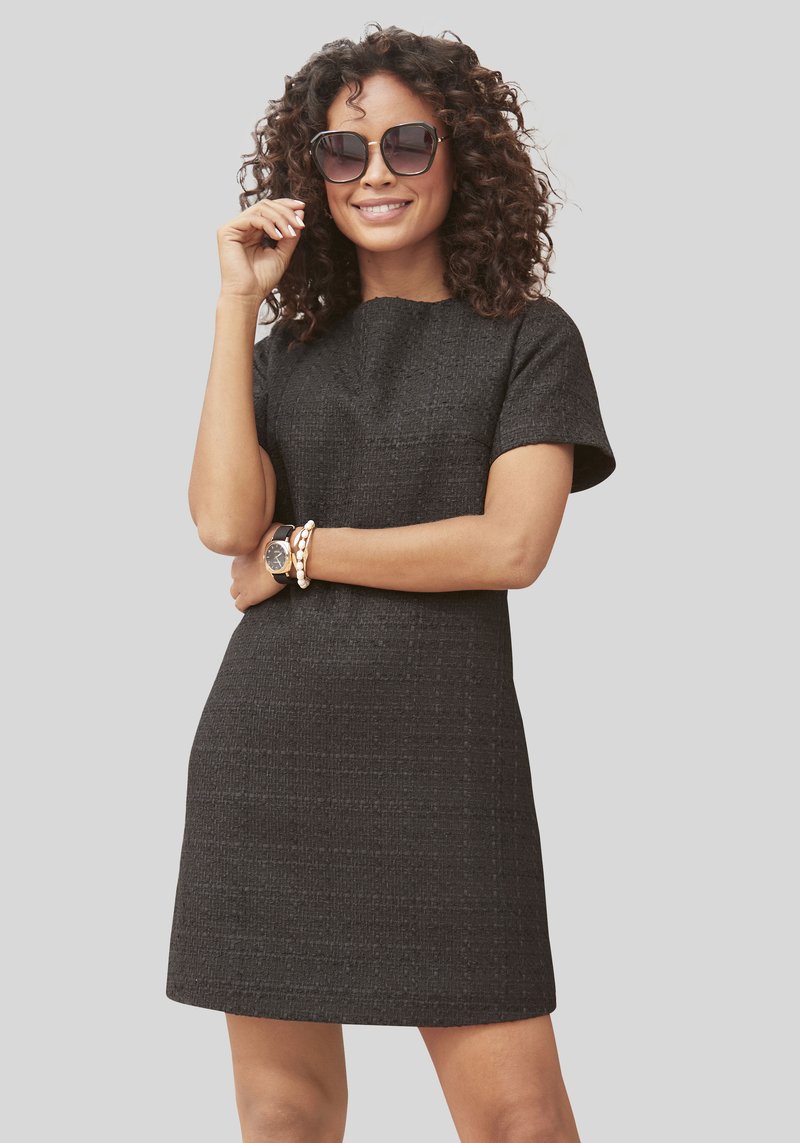 Zwarte textuurovergang met korte mouwen en een ronde halslijn, met een getailleerde silhouet. Model isaccessorized met oversized zonnebrillen en armbanden.